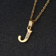 A gold chain necklace featuring a pendant shaped like the letter "J" and adorned with small diamonds is displayed against a dark textured background, embodying a blend of elegance and durability reminiscent of the Stainless Steel Letter Necklace.