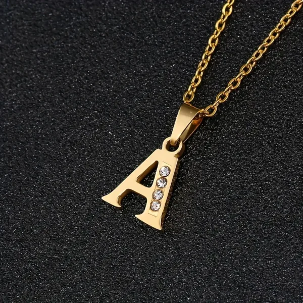 Presenting the Stainless Steel Letter Necklace: a stunning gold necklace featuring a pendant in the shape of the letter "A." It is beautifully adorned with four small diamonds on its right leg and displayed on a black textured background. This elegant piece exudes timeless sophistication, making it a perfect addition to any collection.