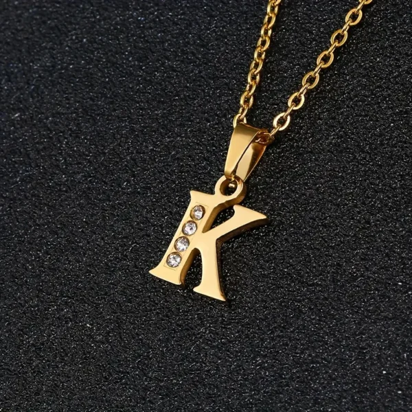 A gold chain necklace featuring a pendant in the shape of the letter "K" from our Stainless Steel Letter Necklace collection. The stainless steel letter is elegantly embellished with four small, sparkling clear crystals arranged vertically along its left side, and it is showcased against a textured black background.