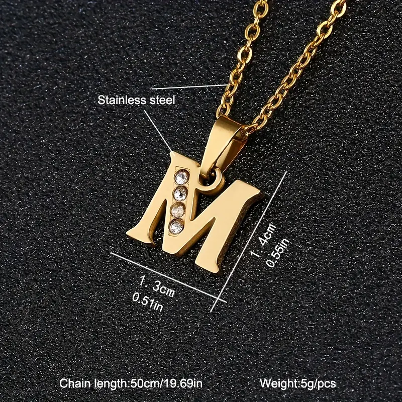 Stainless Steel Letter Necklace featuring a gold-colored finish and an “M” pendant adorned with small rhinestones on the left side. The pendant measures 1.4 cm by 1.3 cm, weighs 5g, and is accompanied by a chain that is 50 cm (19.69 in) long.