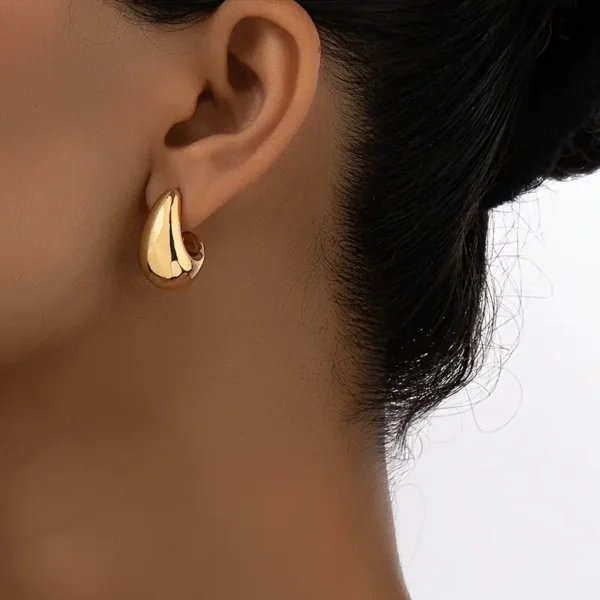 Close-up of a woman's ear wearing the shiny, Geometric Water Drop Earrings. The background is a plain light color. Her hair is pulled back in a neat style, accentuating the delicate water drop earrings that are perfect for daily wear.