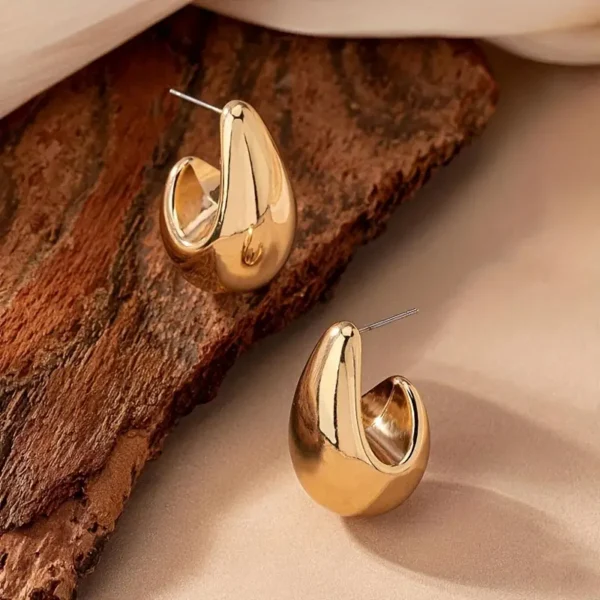 A pair of elegant gold Geometric Water Drop Earrings with a unique, chunky design, displayed on a textured wooden surface. The earrings have a glossy finish and are styled in a way that highlights their modern, geometric form, perfect for daily wear ear jewelry.