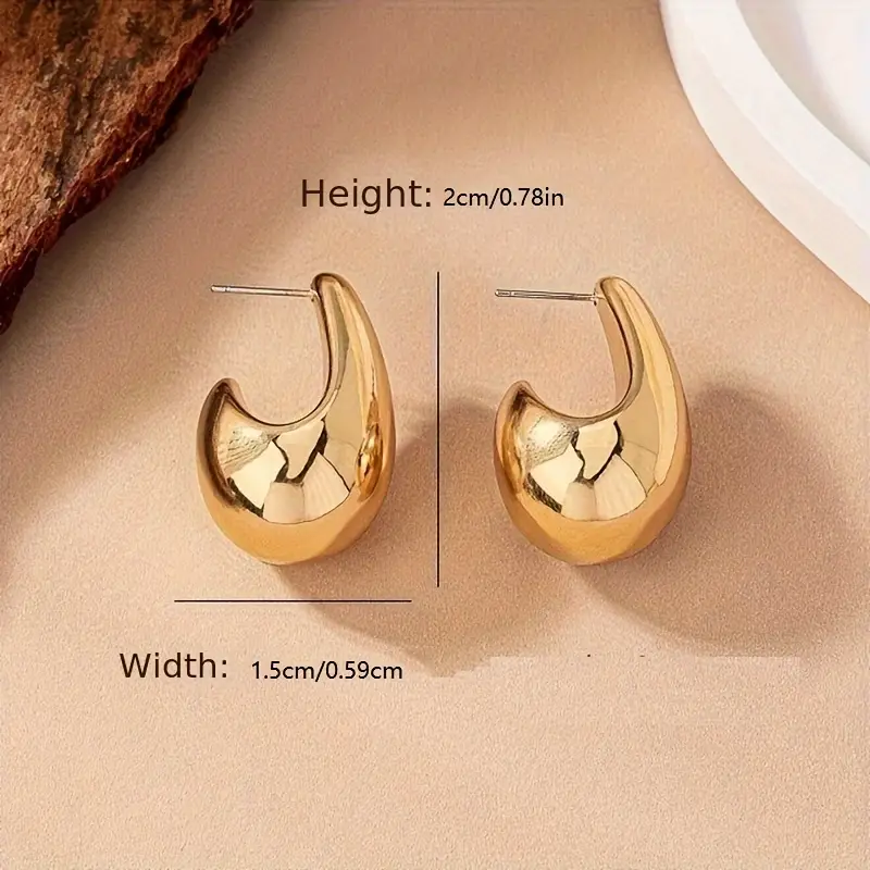 A pair of Geometric Water Drop Earrings featuring a shiny, gold-toned abstract shape with a smooth, curved design. Measuring 2 cm (0.78 in) in height and 1.5 cm (0.59 in) in width, these earrings have a stud fastening and are perfect for daily wear ear jewelry displayed on a beige surface.