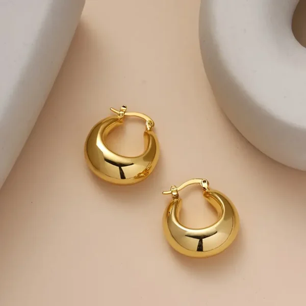 A pair of Elegant French Retro 14K Gold Plated Chunky Hoop Earrings with a minimalist vintage style design, set against a soft beige background. The earrings feature hinged clasps and reflect light beautifully, creating a shiny appearance.