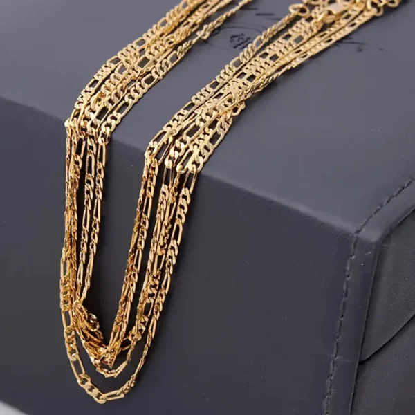 The Gold-Plated 4mm Flat Chain Necklace, known for its sleek and versatile design, is draped over a dark gray box. Its multiple layers and intricate craftsmanship are highlighted against the contrasting background, showcasing the adjustable length of 16-30 inches.