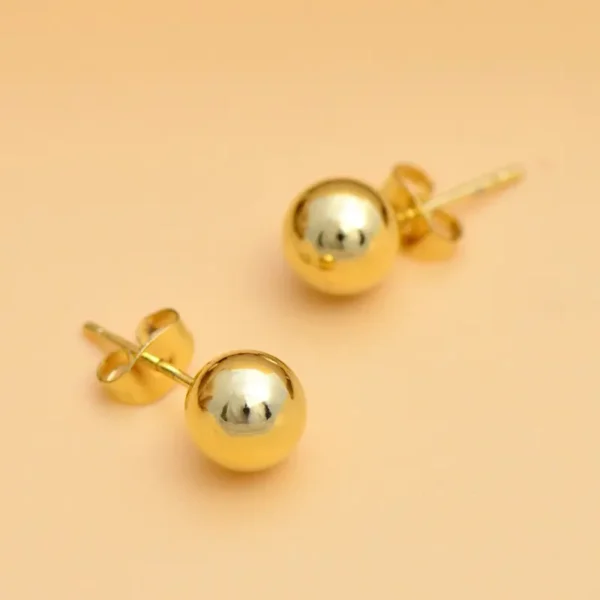 A pair of Stylish 14K Gold Plated Ball Stud Earrings with butterfly backings, set against a neutral beige background. These earrings feature a simple, elegant design with a reflective surface and are the perfect gift for women and girls.