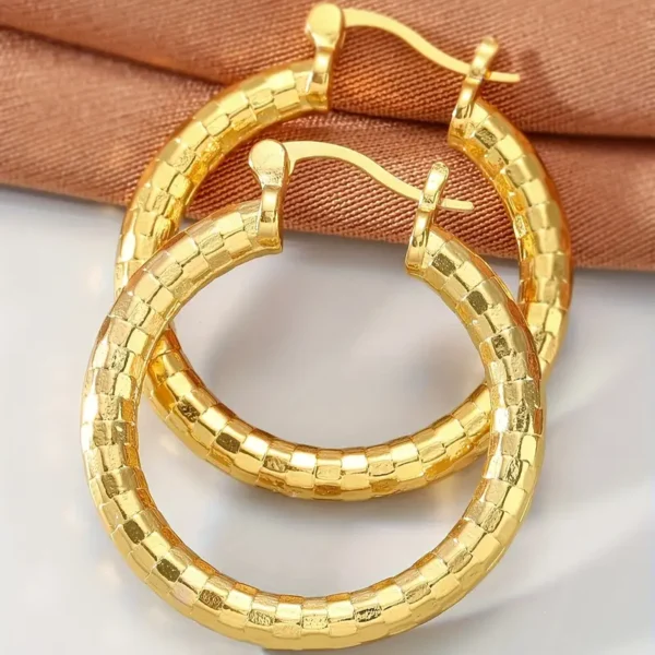 A pair of the 14K Gold Plated Delicate Hoop Earrings - Vintage Bohemian Style are displayed on a soft brown fabric background. These exquisite earrings feature a checkered pattern, polished with a shiny finish and showcasing intricate detailing and craftsmanship.