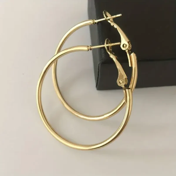 A pair from the 4 Pair Hoop Earrings Set: Minimalist, Stainless Steel, Everyday Chic rests on a black jewelry box. These polished gold stainless steel hoop earrings with latch-back closures showcase a simple and elegant design, ideal for every occasion.