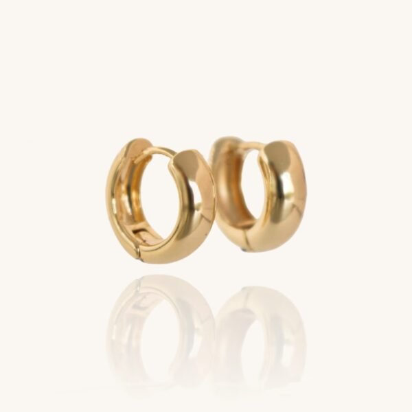 The Chunky Small 14kt Gold Hoops Earrings are displayed against a plain, light background. Each earring features a smooth, rounded design and is slightly open. Their shiny, reflective surface creates a mirrored image below them, showcasing the elegance of these gold huggies.