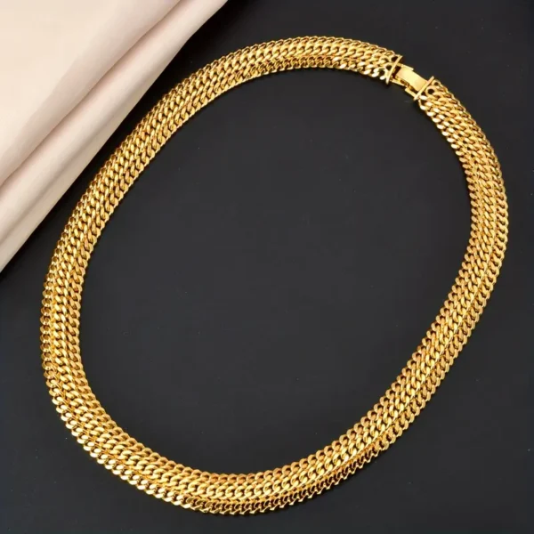 The Hip Hop Miami Cuban Necklace and Bangle Earrings Set features a gold necklace with a thick, interwoven link design, elegantly displayed against a black background with beige fabric partially draped in the top left corner. This unisex fashion jewelry piece boasts a polished finish and comes with a secure clasp.