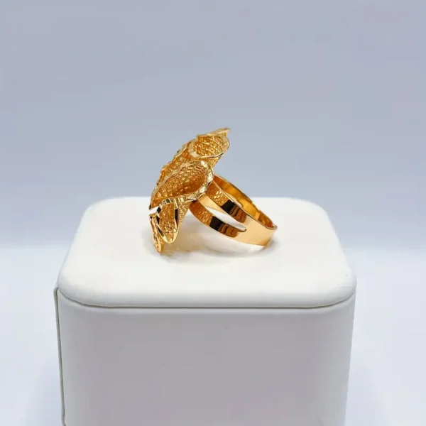 An Exquisite Flower Open Ring, crafted from golden luxury copper and perfect for romantic gifts, is displayed on a white cushioned stand. This ring features an intricate design with textured, detailed motifs resembling leaves or feathers, giving it a unique and elegant appearance against the plain background.