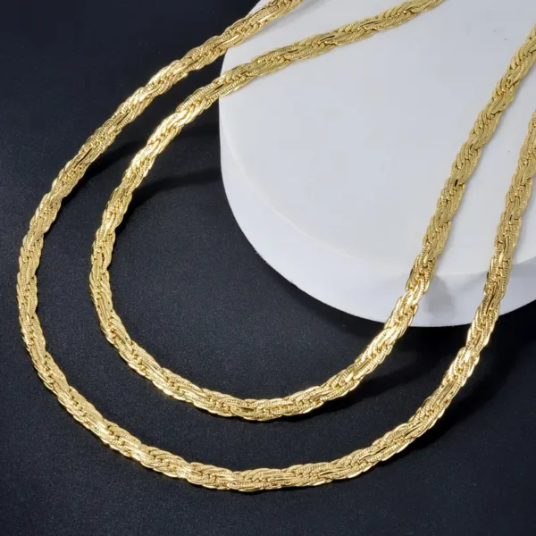 A close-up image of two intricately designed Golden Chain 0.2 inch Wide Long Geometric Necklaces displayed on a black background. The chains, resembling a dainty gold necklace gift, are laid out in an elegant curve, showcasing their detailed texture and craftsmanship. One chain rests on a white, circular surface, adding contrast to the composition.