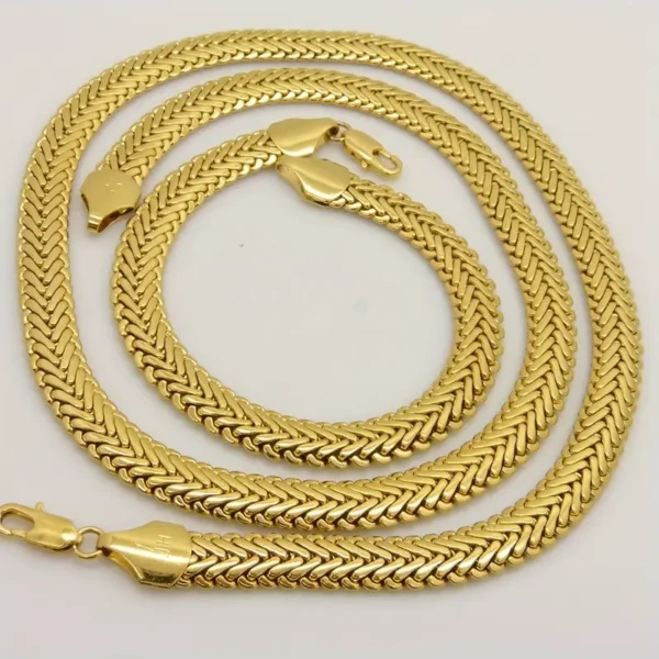 A set of two intertwined yellow gold chains, one longer than the other, placed side by side against a white background. The herringbone chains, from the stylish "Hip Hop Royalty: Gold Plated Herringbone Set," feature sleek clasps that showcase their polished and elegant design—ideal for hip hop jewelry aficionados.