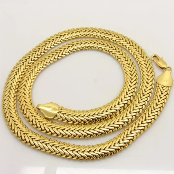 A long, intricately woven Hip Hop Royalty: Gold Plated Herringbone Set necklace is coiled neatly on a light-colored surface. This piece of hip hop jewelry features a shiny, polished finish and has a clasp marked with "JH" at one end.