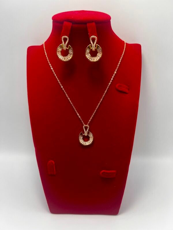 A 3-piece gold-plated jewelry set, consisting of a necklace and earrings, is elegantly displayed on a red velvet stand. Crafted from stainless steel and adorned with cubic zirconia, the luxurious set features intricately detailed circular gold designs. The vibrant red background makes the women's jewelry set truly stand out.