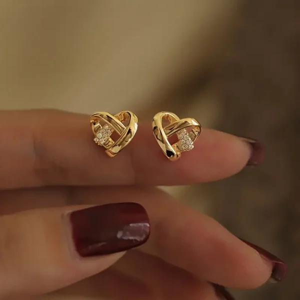 a pair of gold heart shaped earrings on a finger