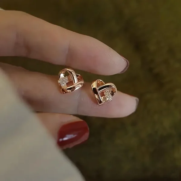 a hand with a pair of gold heart earrings